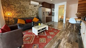 Una sala de estar con un sofá, una mesa de centro y un tapete estampado. Se observa una zona de cocina con armarios y un microondas.