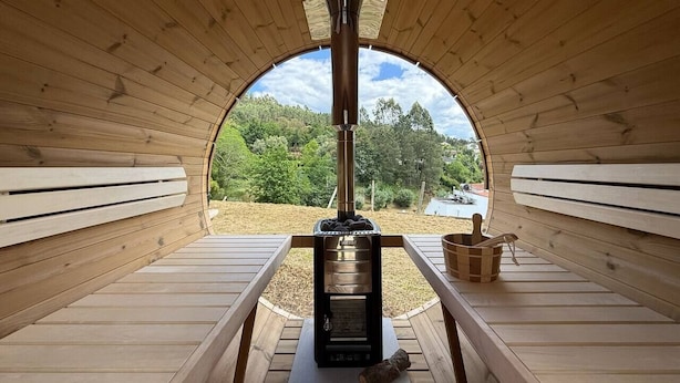 Una cabaña de madera con un horno de leña en el centro, bancos a ambos lados y vistas al exterior.