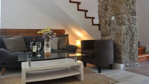 Una sala de estar moderna con una pared de acento de piedra, una escalera y un sofá con una mesa de centro de vidrio.