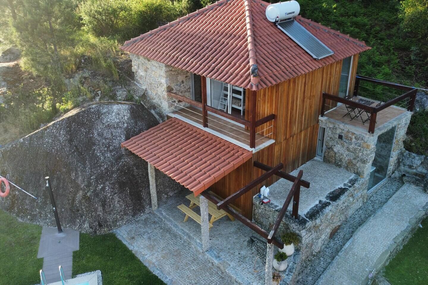 Una cabaña de madera con techo de tejas rojas, un balcón y una pequeña terraza.