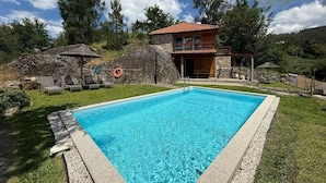Una piscina rectangular con borde de piedra, rodeada de césped y un muro de piedra.