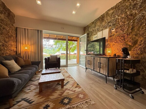A living room with a sofa, coffee table, and TV stand. There is a stone wall and a sliding glass door leading to a balcony.