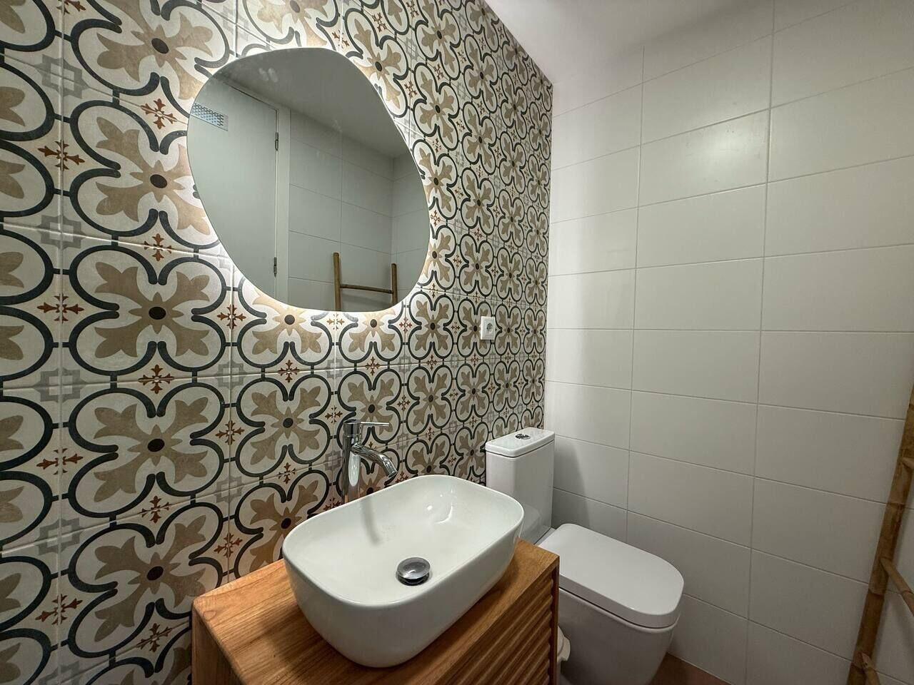 Un baño con pared de diseño, un espejo redondo, un lavamanos y un inodoro.