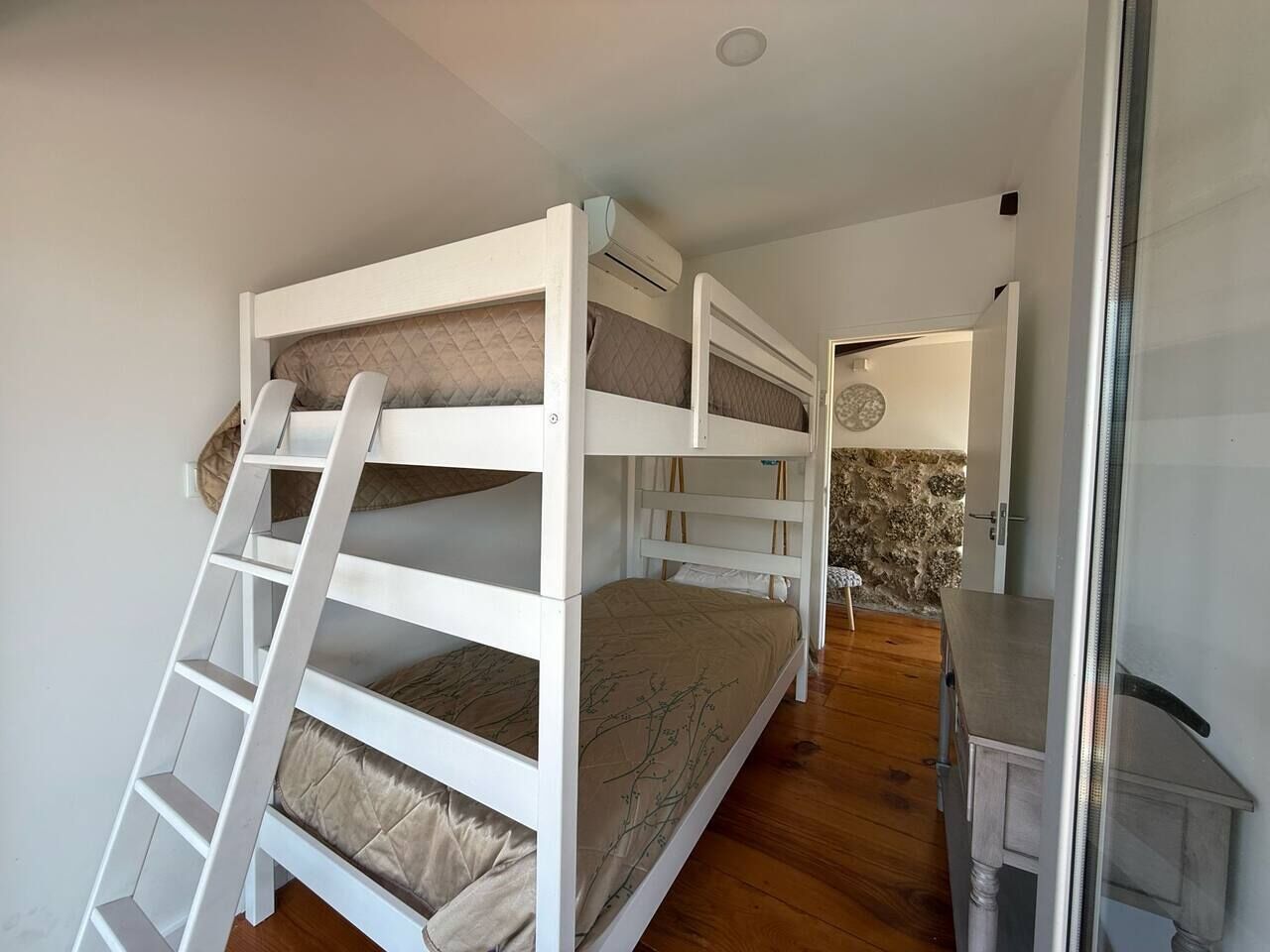 A bunk bed room with a ladder, a small table, and a wall-mounted air conditioning unit.