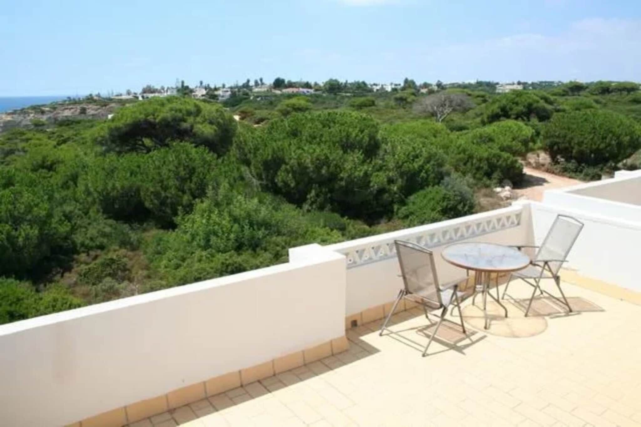 A terrace with a table and chairs, overlooking a lush green landscape and a distant coastline.