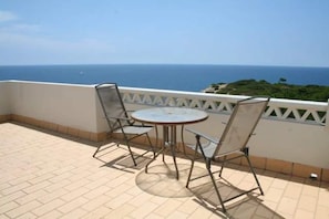 Eine Terrasse mit Tisch und Stühlen, mit Blick auf das Meer.
