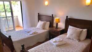 Une chambre d’hôtel avec deux lits, chacun doté d’une tête de lit en bois et de linge de lit blanc. Il y a une table de chevet avec une lampe entre les deux lits, et une fenêtre donnant sur l’extérieur.