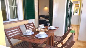 Une table de salle à manger en bois, mise avec des assiettes, des bols et des couverts, est placée dans une pièce dotée d’une porte verte et d’une fenêtre avec des volets blancs.