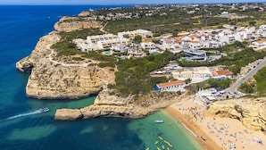 A coastal town with buildings on a cliff, a beach, and clear blue sea.