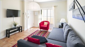A living room with a grey sofa, red armchair, and a flat-screen TV mounted on the wall. - Apartment with beautiful terrace, sea-views (Benagil)