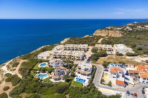 An aerial view of a coastal residential area with multiple apartment buildings, a swimming pool, and a lighthouse in the background. - Apartment with beautiful terrace, sea-views (Benagil)