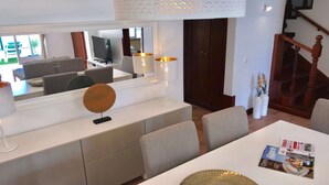 A modern dining area with a white table, chairs, and a magazine on the table. There is a large mirror above the table and a staircase in the background. - Family-Friendly Villa in Benagil (Benagil)