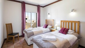 A hotel room with two beds, a chair, a nightstand with a lamp, and a view of a balcony. - Holiday home near Praia de Benagil beach (Benagil)