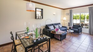 A living room with a dining table, sofa, and chairs. There is a window with curtains, a lamp, and a mirror on the wall. - Holiday home in Benagil with communal pool (Benagil)