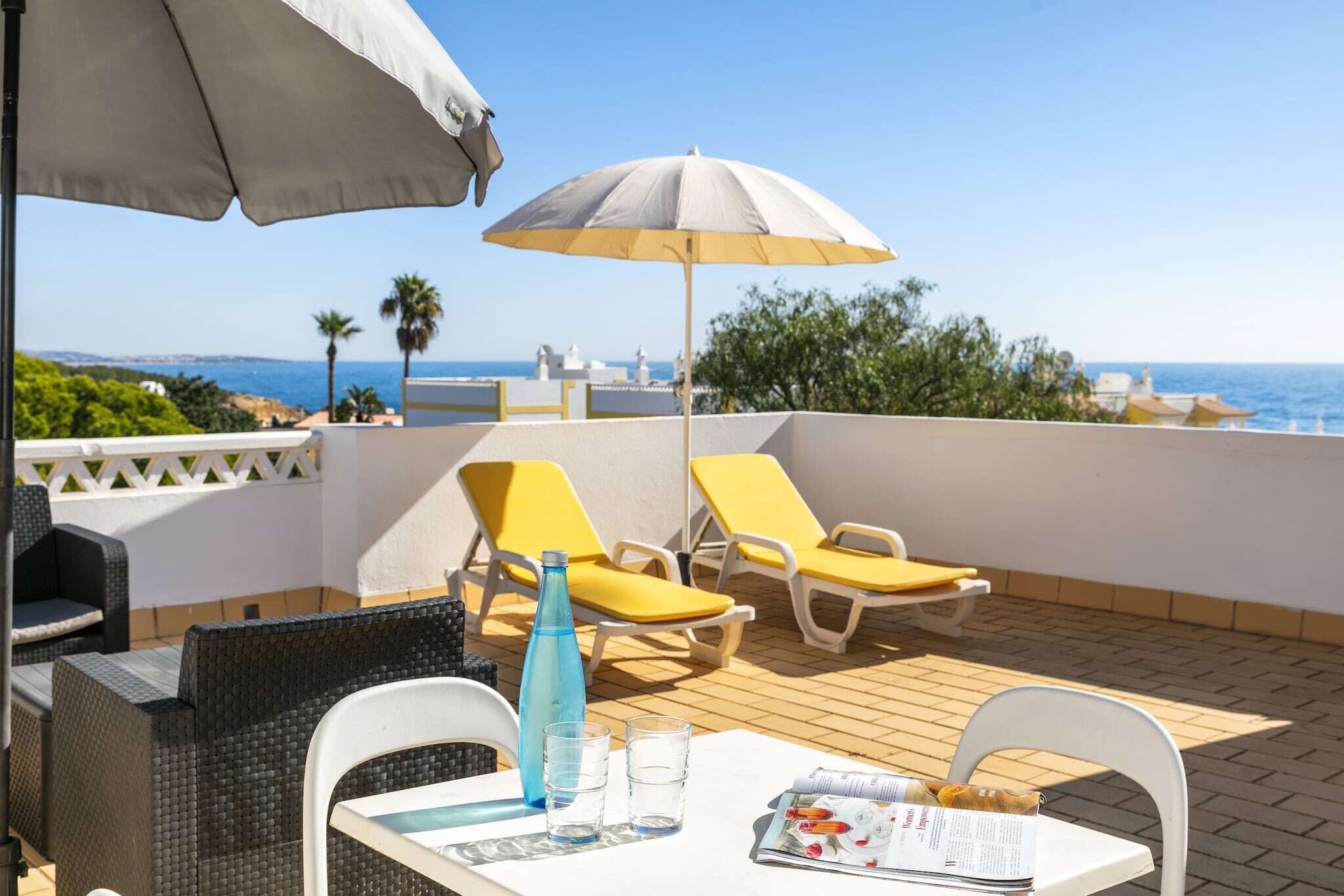 A terrace with yellow lounge chairs, a table with drinks, and a view of the sea.