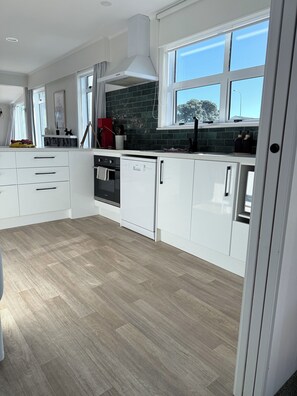 A modern kitchen with white cabinetry, a dishwasher, and a window with a view of the sky.