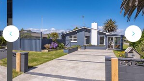 A modern two-story house with a large front yard, a garage, and a small garden area. - Palm Haven Beach Retreat (Paraparaumu Beach)