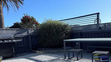 A wooden deck with a grill, seating, and potted plants.