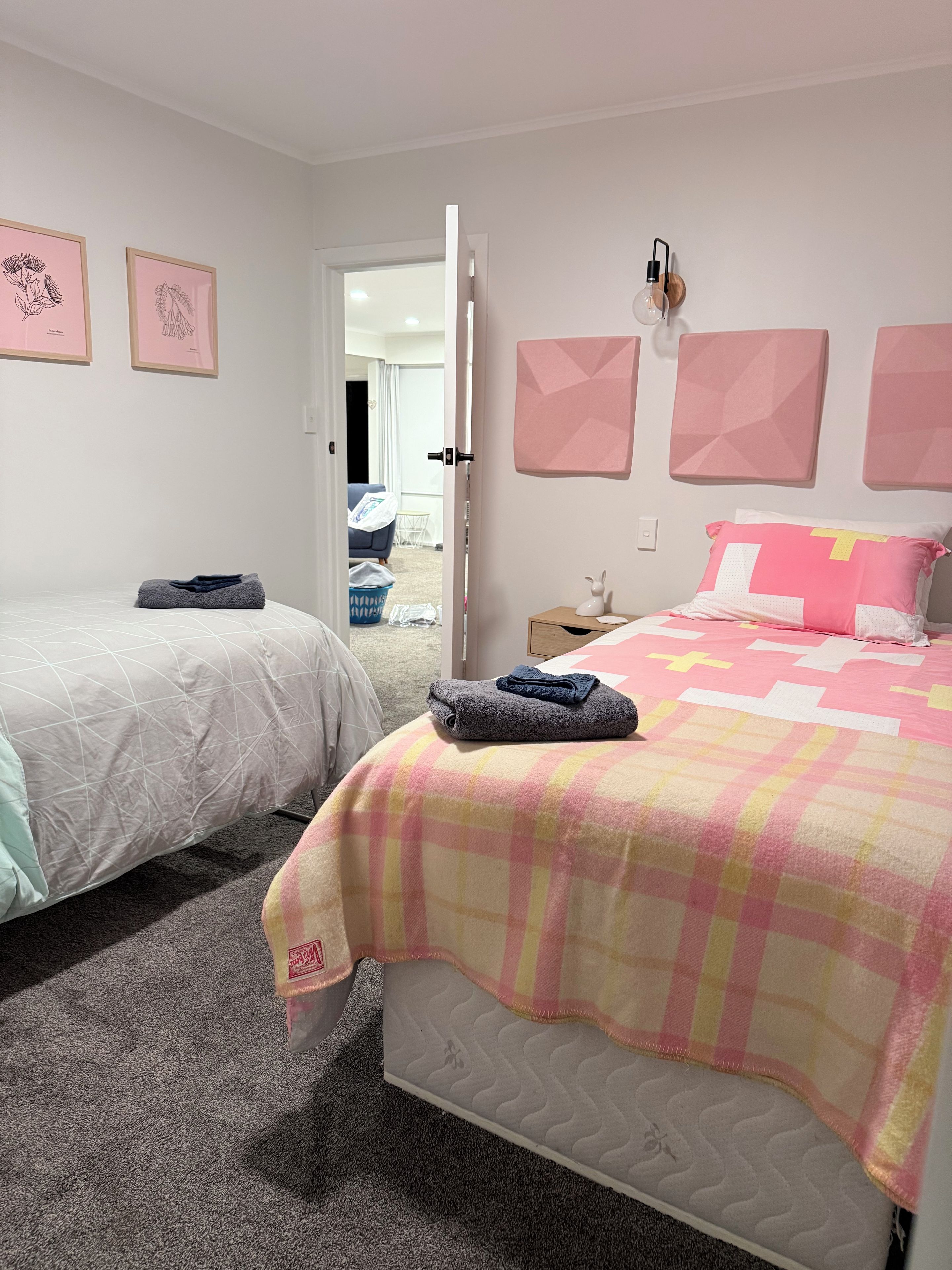 Un dormitorio con dos camas, una puerta que da al baño y una pared decorada con cuadros.
