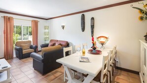 Una sala de estar con sofá, una mesa de comedor con sillas y una ventana con cortinas.