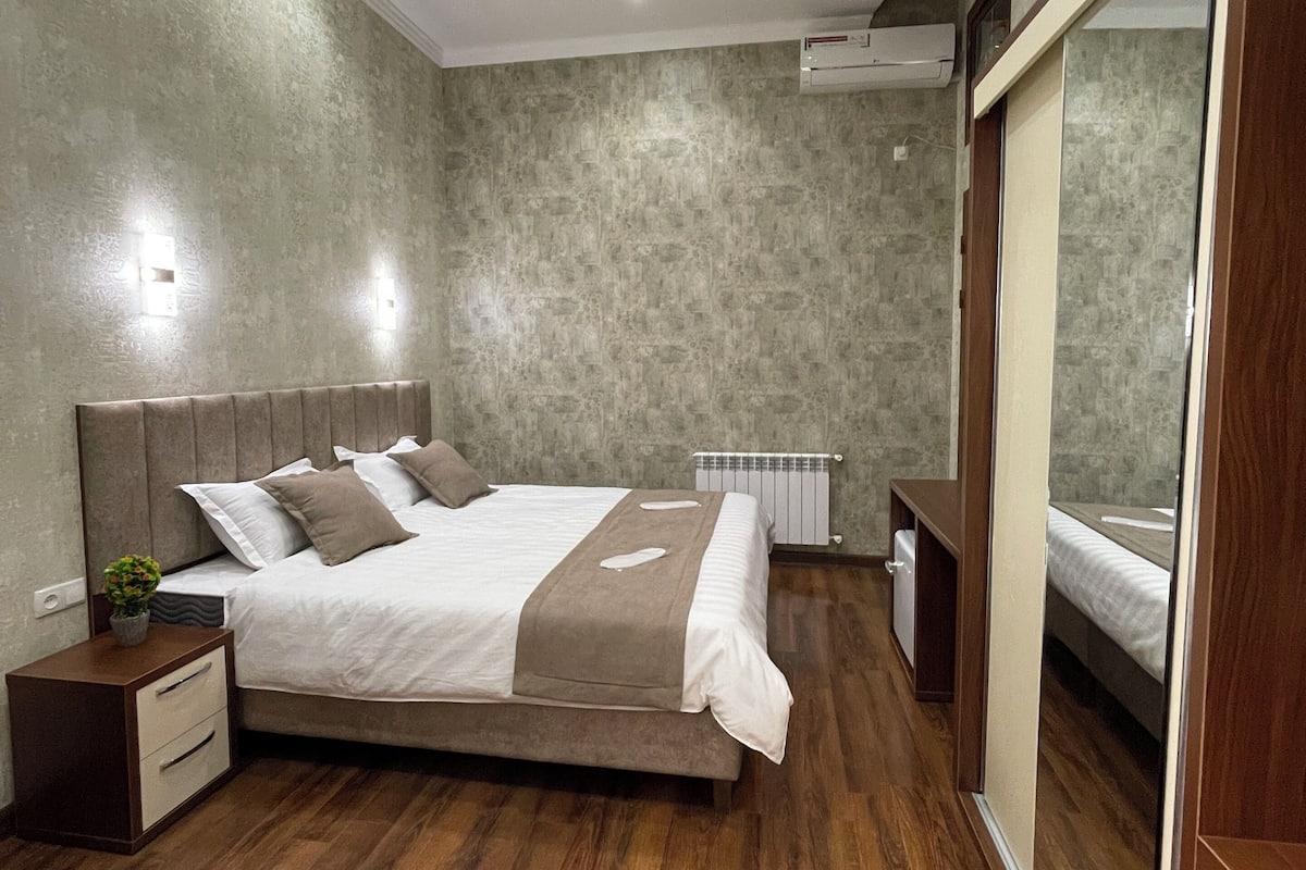 A modern bedroom with a large bed, wooden flooring, a built-in wardrobe, and a ceiling with a circular design.