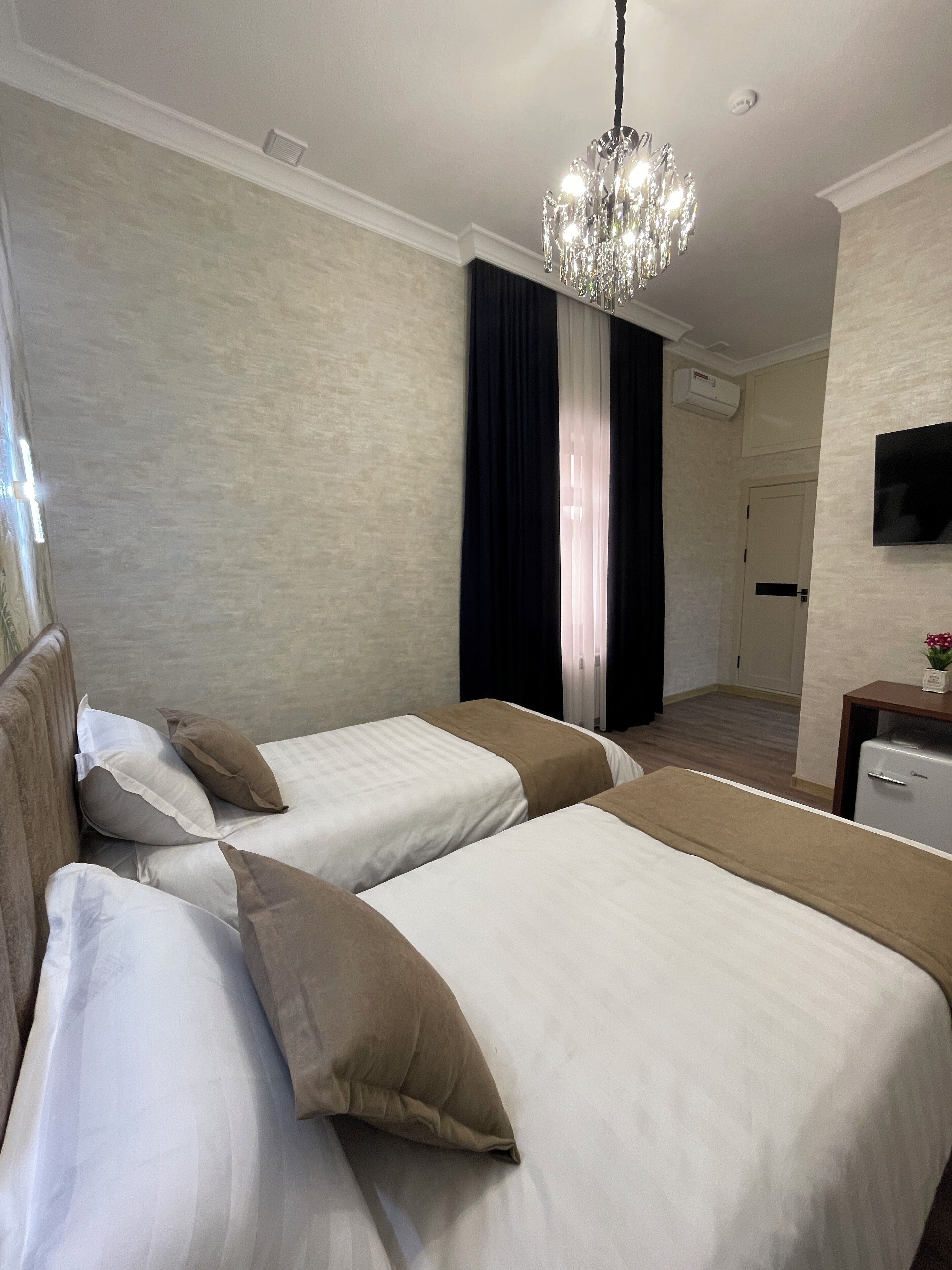A hotel room with two beds, a chandelier, a television, and an air conditioning unit.