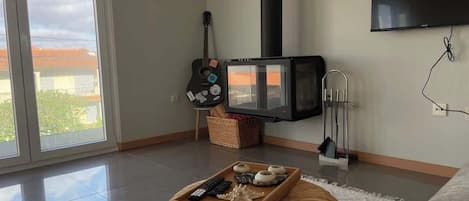 A modern living room with a large window, a flat-screen TV, a guitar, and a tray with remote controls and a starfish.