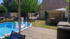 Un jardin avec une piscine, une terrasse en bois et un espace clôturé, avec une maison en arrière-plan.