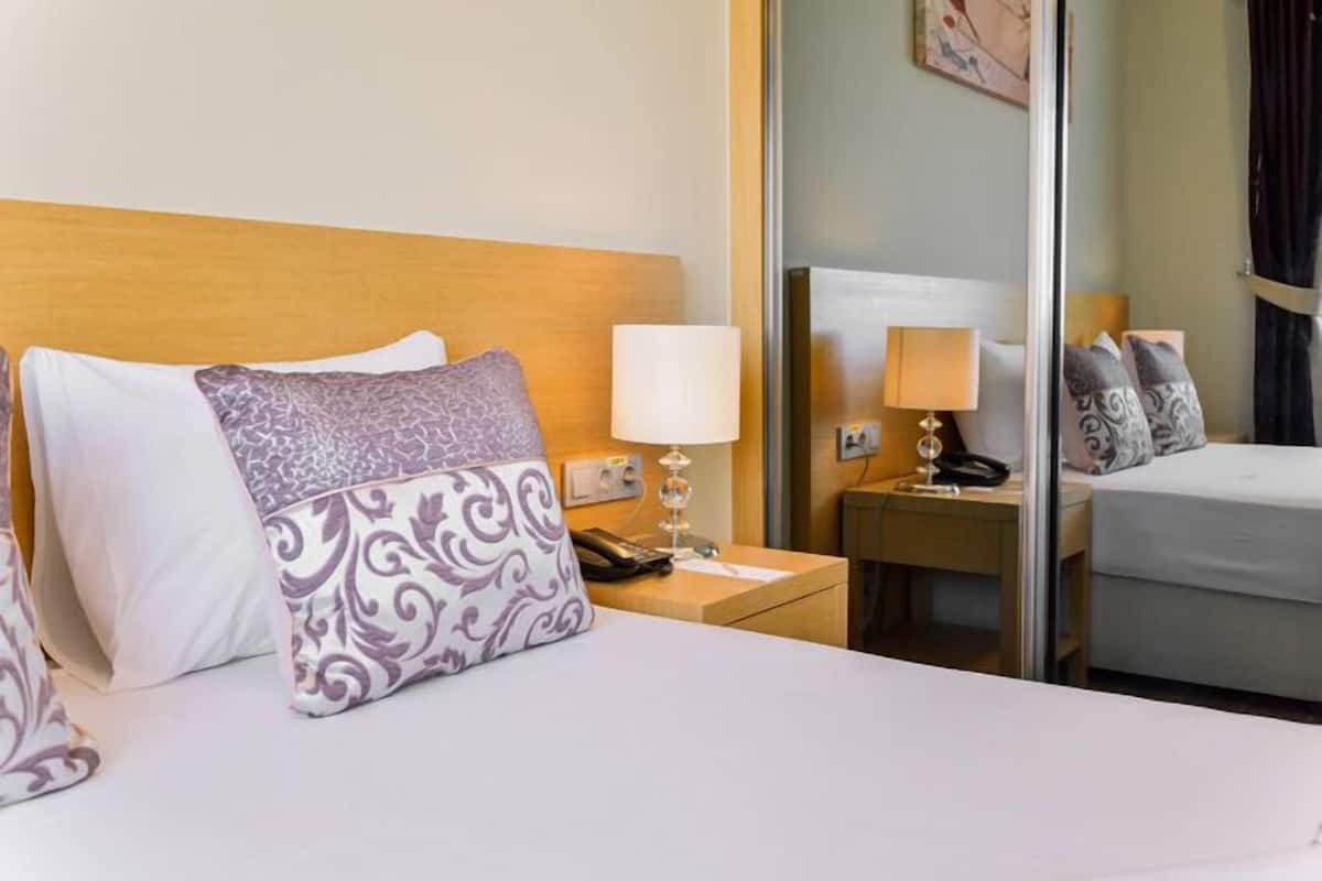 A hotel room with a bed, two bedside lamps, a nightstand, and a mirror.