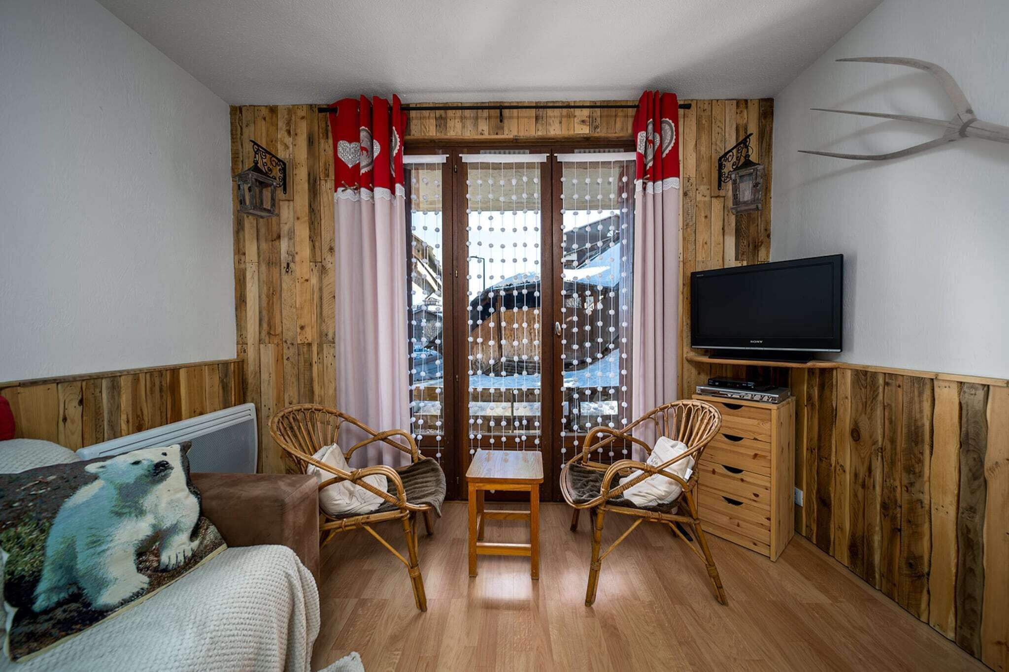 A cozy room with wooden walls, a television, two wicker chairs, a small table, and a polar bear pillow.