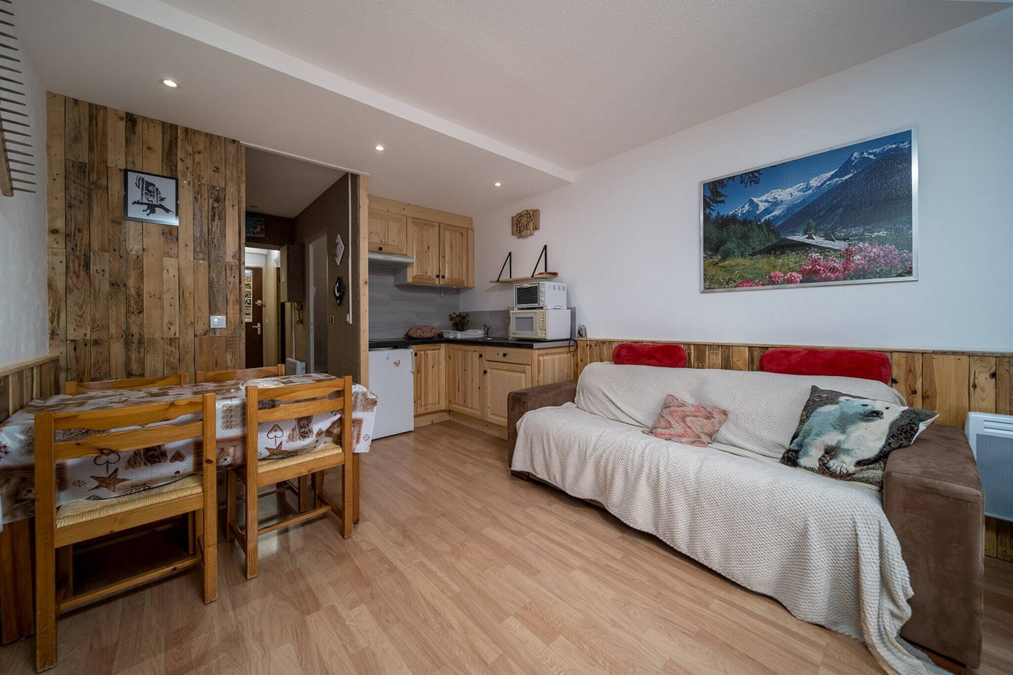 Een gezellige kamer met een houten eettafel, een bank en een keukenhoek met houten kasten en een magnetron.