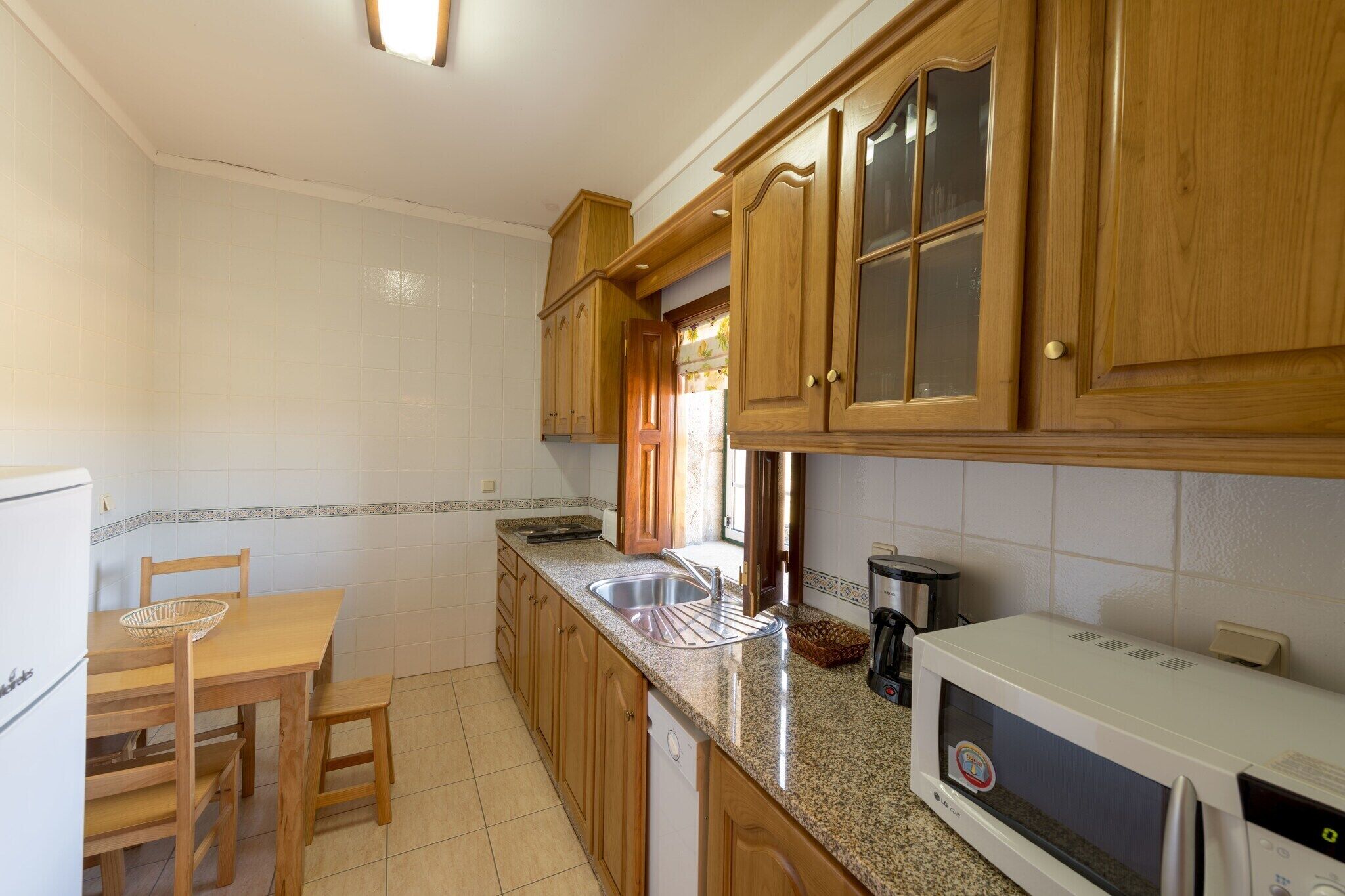 A kitchen with wooden cabinets, a granite countertop, a white refrigerator, and a microwave.
