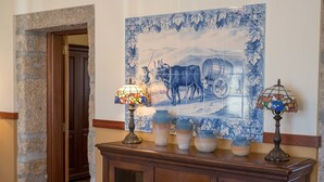 Une pièce avec un mur en pierre, une porte en bois, une fresque murale en carreaux, un meuble en bois orné de vases et une table avec une chaise.