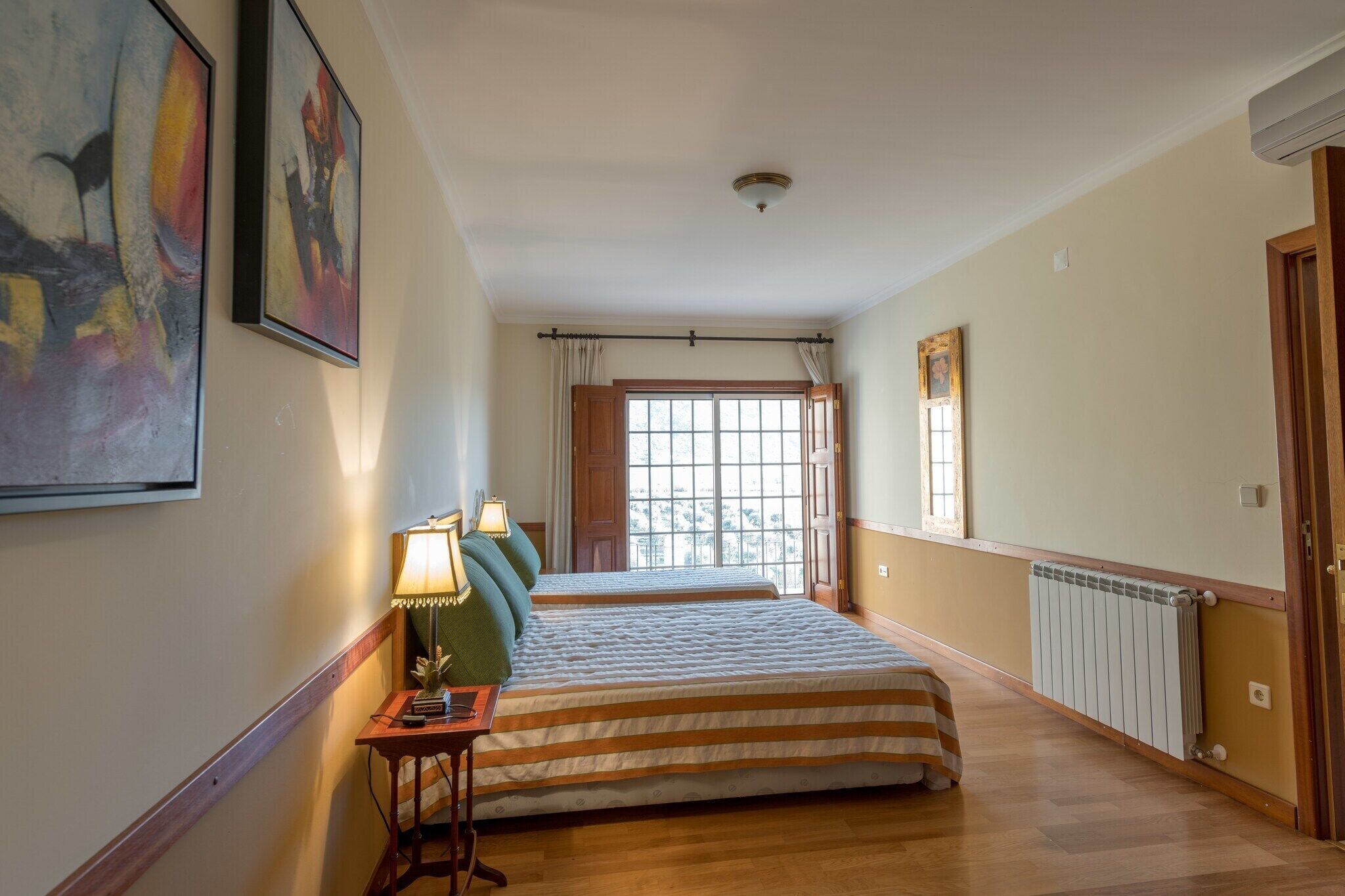 Ett hotellrum med två sängar, ett fönster med gardiner, ett element och en väggmonterad luftkonditioneringsanläggning.