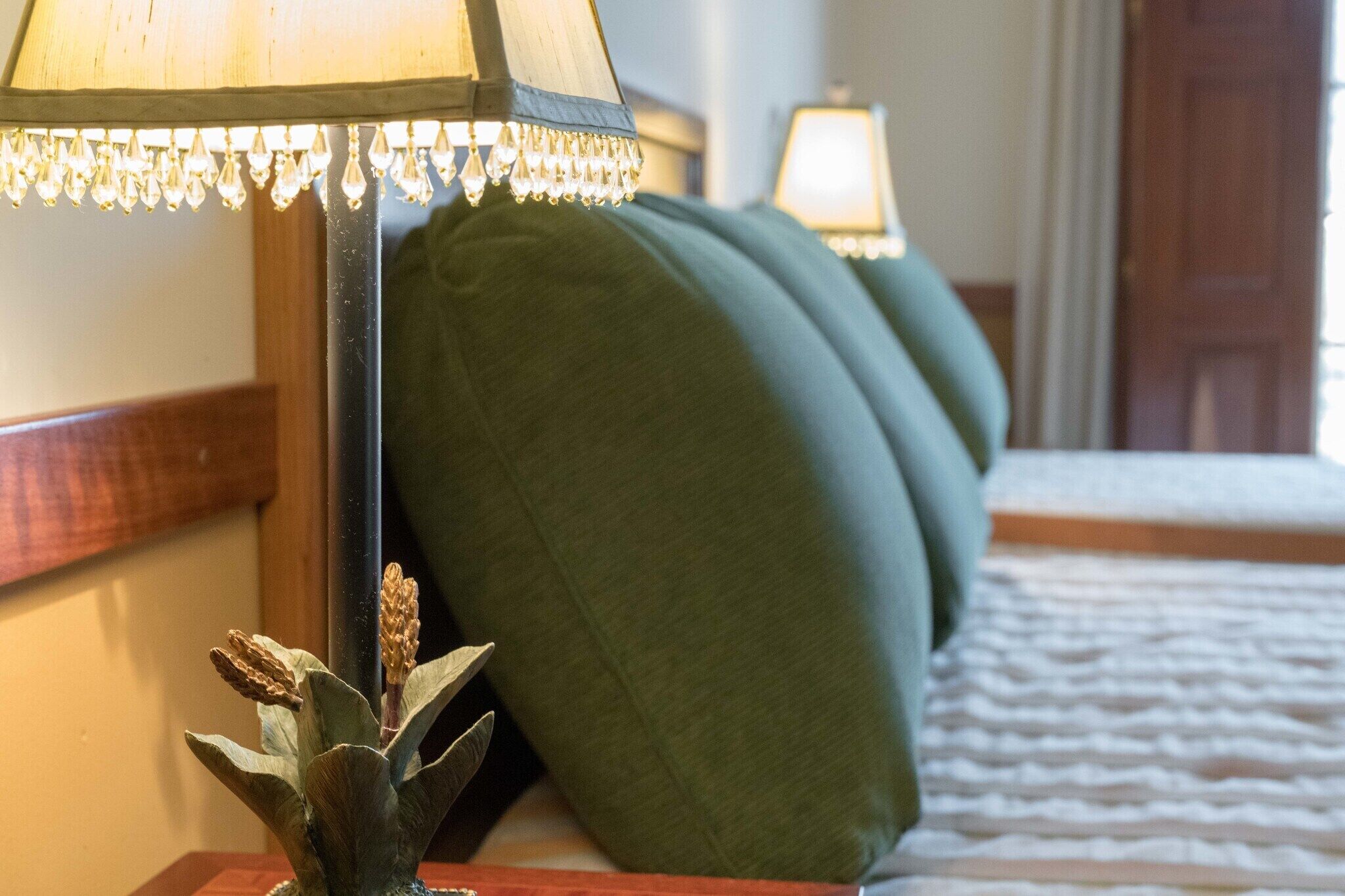 Una cama con almohadillas verdes y una lámpara con pantalla decorativa.