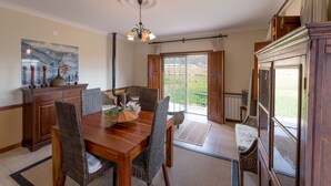 A dining area with a wooden table, wicker chairs, a chandelier, and a view of the outdoors through a glass door. - Cozy Cottage with Swimming Pool (Vila Flor)