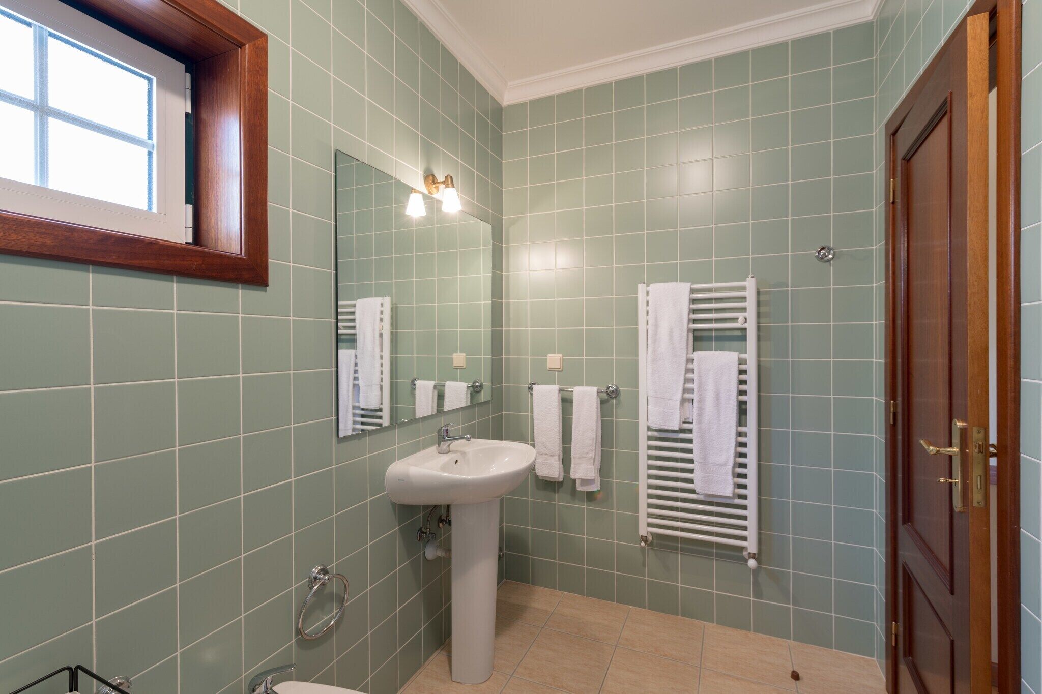 Une salle de bain avec des carreaux verts, un lavabo blanc, un miroir et un porte-serviettes.