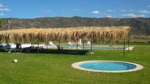 A pool area with a circular pool, lounge chairs, and a thatched roof structure. - Cozy Cottage with Swimming Pool (Vila Flor)