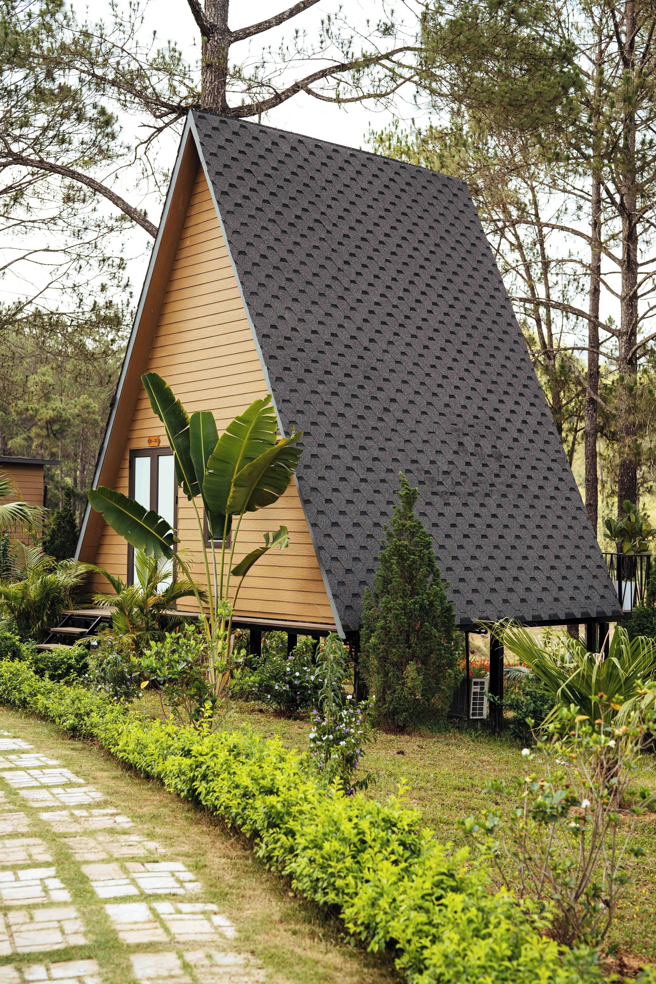 A triangular-shaped building with a sloped roof, surrounded by lush greenery and a stone pathway.