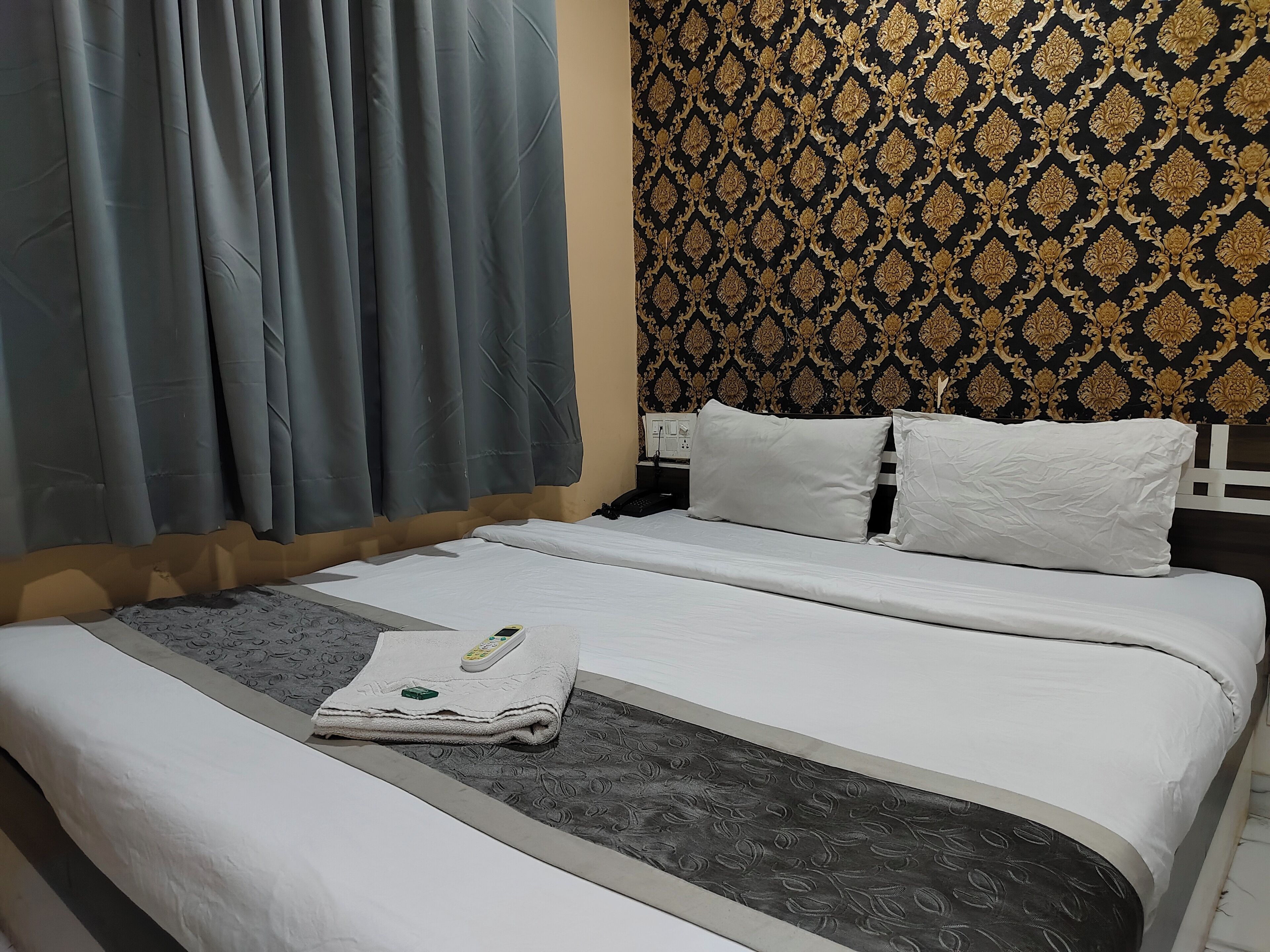 Una cama bien hecha con sábanas blancas, una toalla doblada y un control remoto sobre la cama.