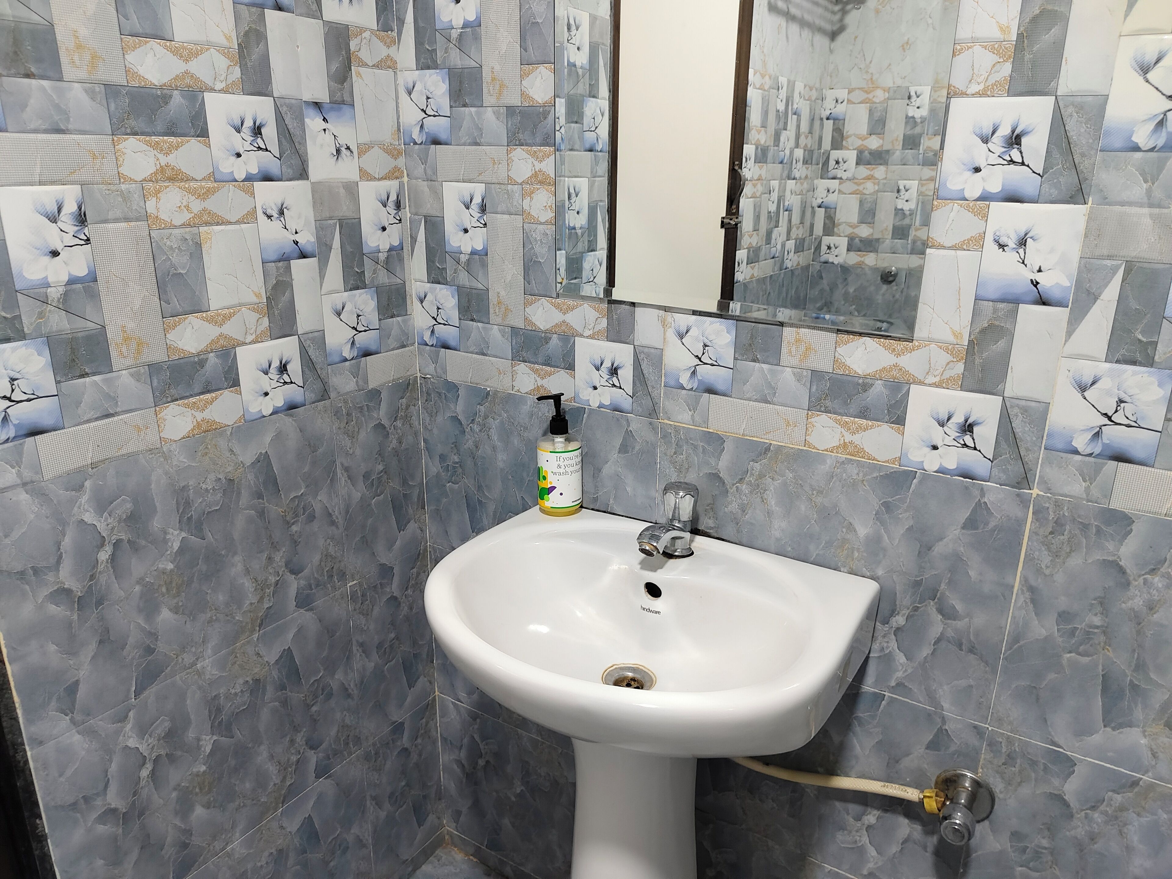 Un baño con un lavabo pedestal blanco, un dispensador de jabón de mano y un espejo sobre el lavabo.