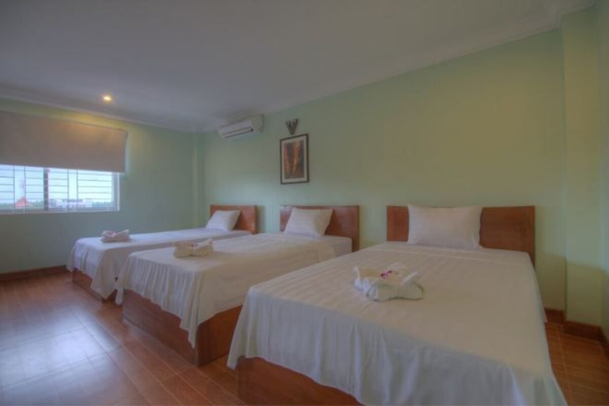A hotel room with three single beds, a window with blinds, an air conditioning unit, and a framed picture on the wall.