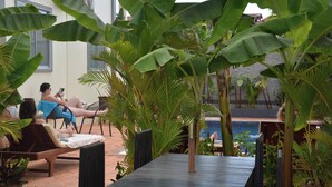 A poolside area with lounge chairs and a table, surrounded by large banana plants and other greenery. - Domnak Soksan Boutique (Siem Reap)