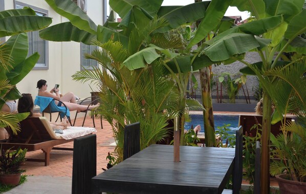 A poolside area with lounge chairs and a table, surrounded by large banana plants and other greenery.