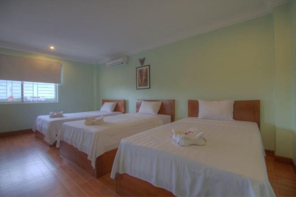 Habitación de hotel con tres camas, una ventana y un cuadro en la pared.