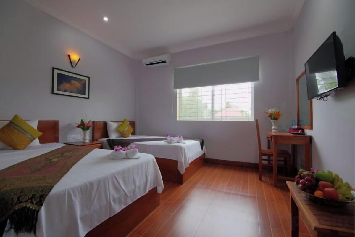Habitación de hotel con dos camas, televisión, ventana y una mesa con fruta.