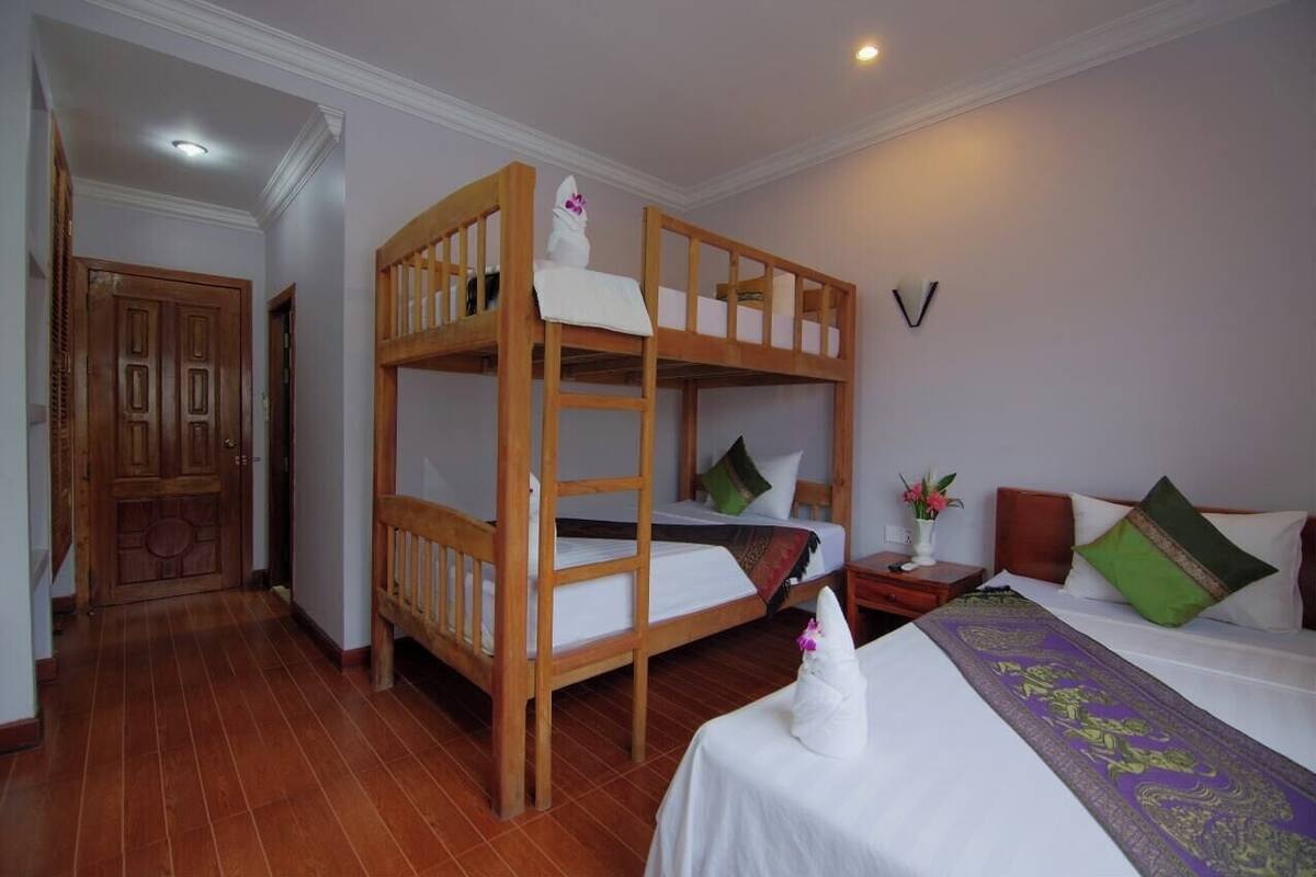 Een kamer met een stapelbed, een bed met decoratieve dekbedovertrek, een nachtkastje met een vaas bloemen, en een houten deur.