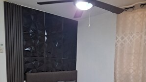 Un dormitorio con cama, mesita de noche, ventilador de techo y ventana con cortinas.