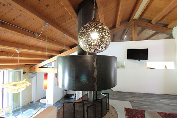 A modern interior with a large metallic sculpture, wooden ceiling beams, and a flat-screen TV mounted on the wall.