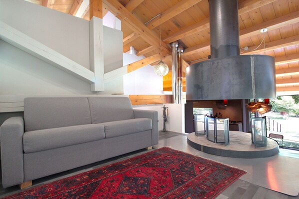 A modern living room with a grey sofa, a red patterned rug, and a large fireplace with a chimney.